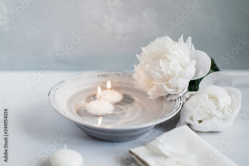 Burning little candles inside porcelain bowl filled with water close to fresh flowers photo