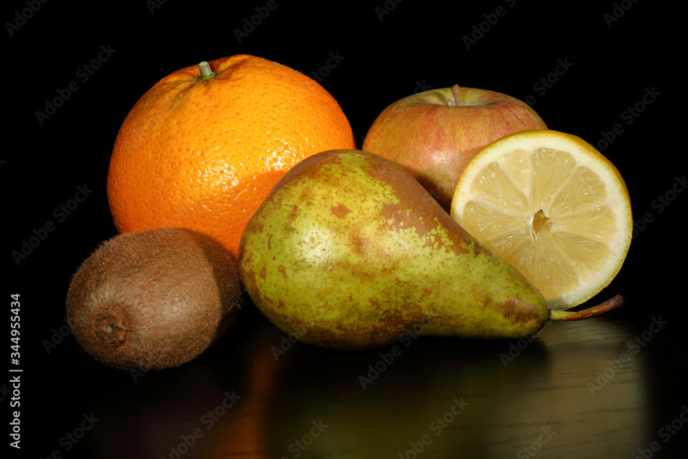 Fruit still life with a black background consisting of a pear, an orange, a kiwi, an apple and a split lemon with horizontal framing. Five fruits a day