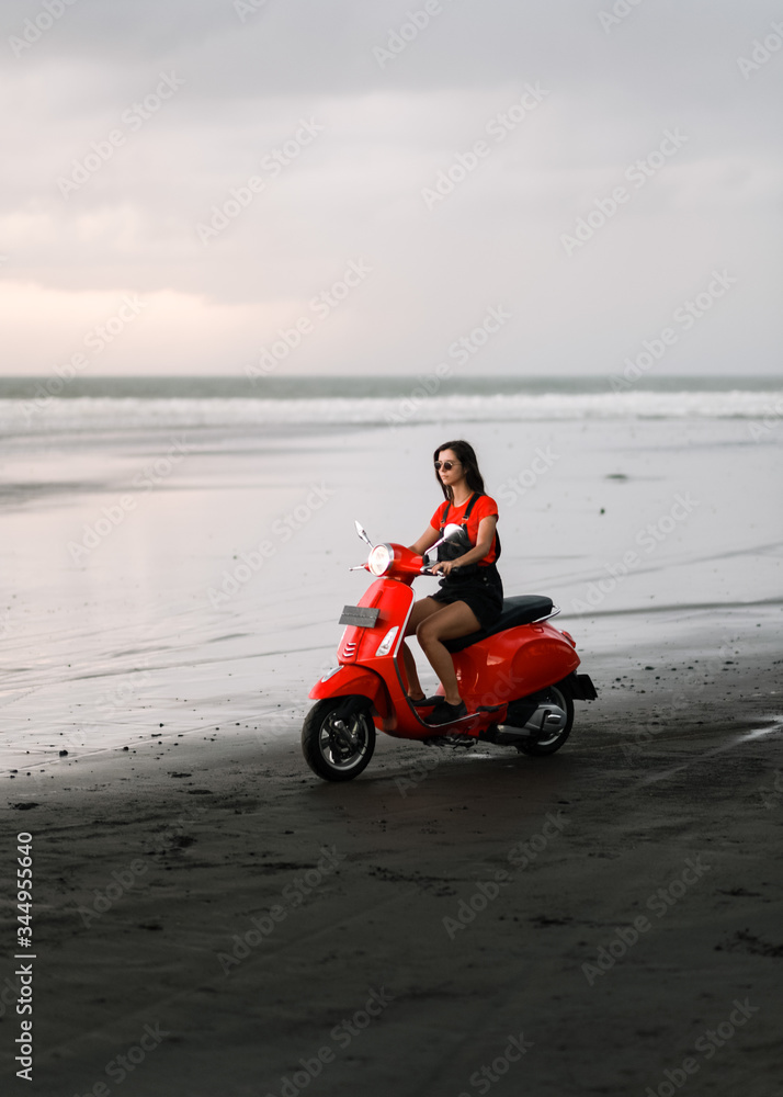 young girl riding a red scooter along the ocean, summer warm evening young girl riding a red scooter along the ocean, summer warm evening