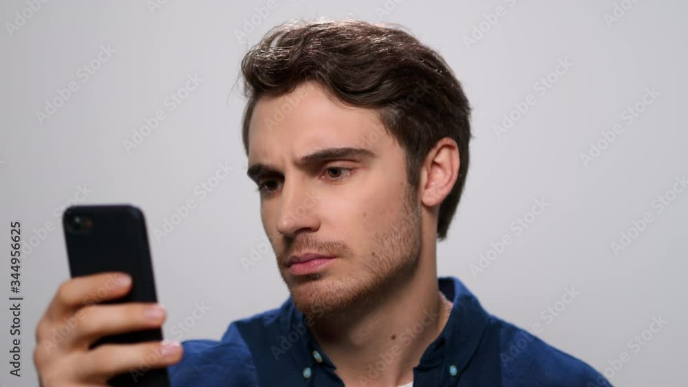 Upset man reading bad news on smartphone. Sad guy using phone in studio Upset man reading bad news on smartphone. Sad guy using phone in studio
