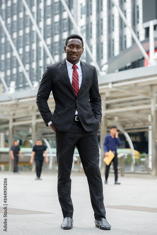 Young handsome African businessman standing in front of modern building at Bangkok city Young handsome African businessman standing in front of modern building at Bangkok city
