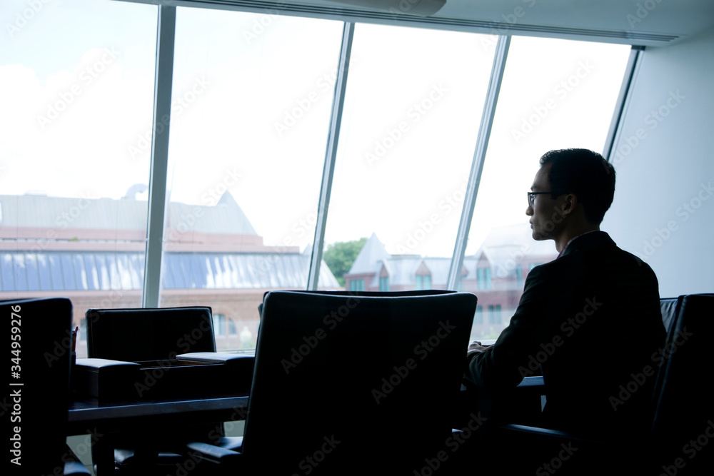 Thoughtful businessman looking through window while sitting in conference room Thoughtful businessman looking through window while sitting in conference room