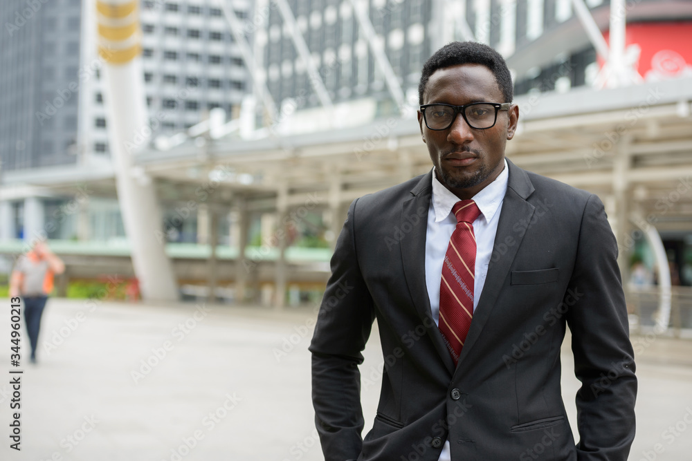 Young handsome African businessman standing in front of modern building at Bangkok city