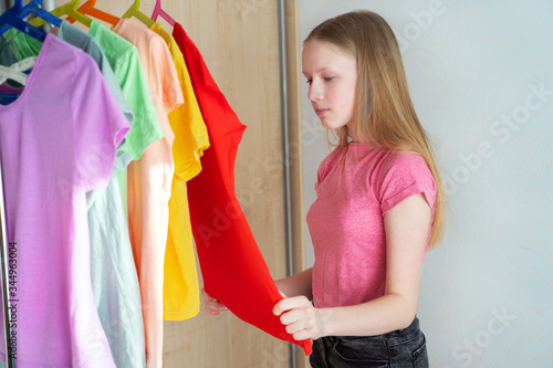 Young girl choosing outfit from wardrobe closet with different colors of t shirts hung under the colors of the rainbow