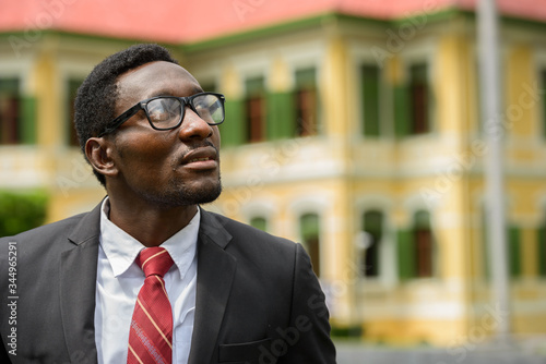Happy young African businessman with eyeglasses thinking in the city streets outdoors