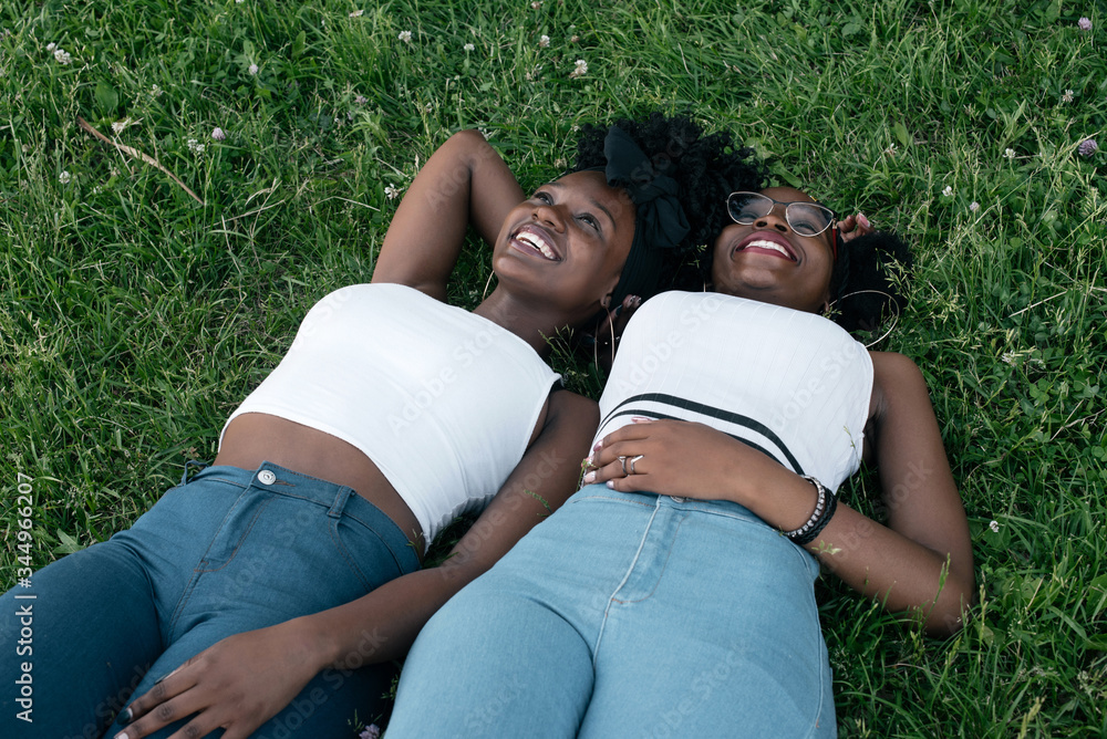 Two african girls in jeans and white tops are laying on the grass Stock Photo | Adobe Stock