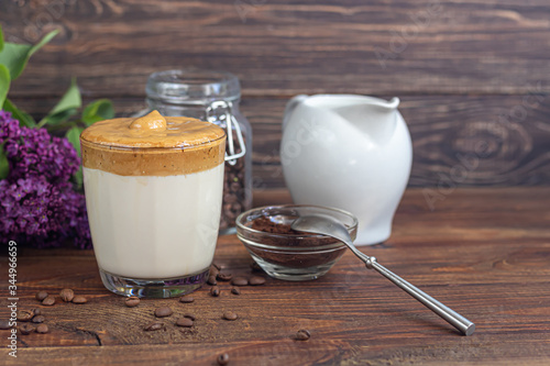Dalgona coffee is a trendy cold Korean drink. Tasty, aromatic coffee with milk and sugar in a glass on a wooden background.