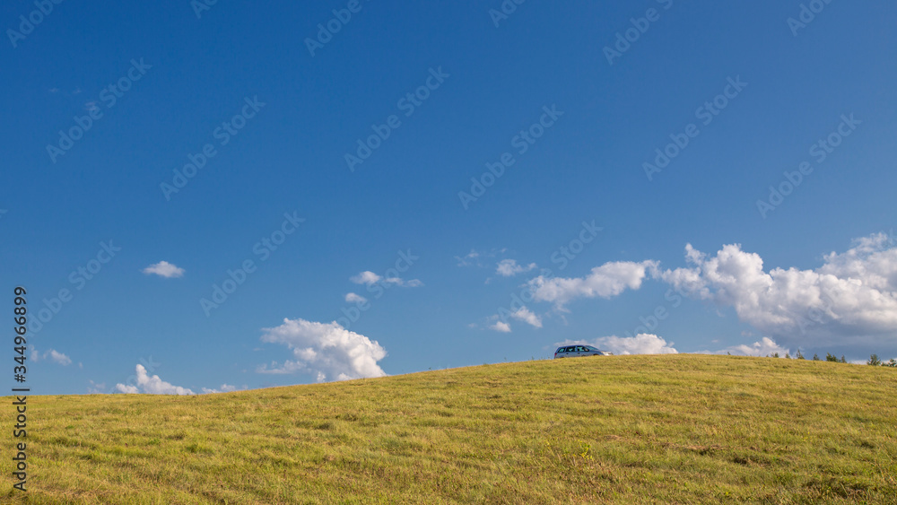 sloping meadow on a hillside, at the top is a car