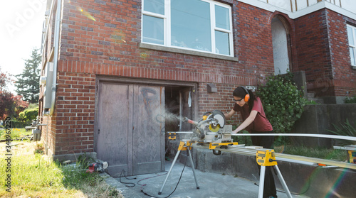 Young woman using chop saw to cut baseboard trim photo