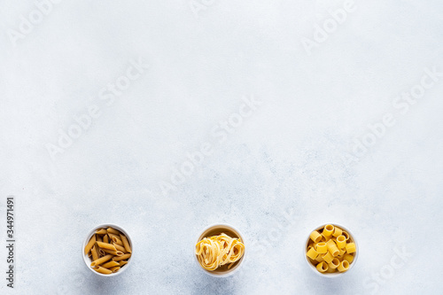 Various types of Italian pasta in craft cups are on the gray table. Penne, tortellini, fusilli and Farfalle. Copy space. Horizontal.