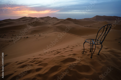 A chair on the top of a dune in the desert placed to enjoy the sunset.