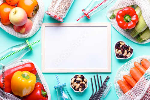 White board for meal plan or diet strategy with fresh vegetables and fruits in mesh bags on blue table top. Zero waste accessories, leading healthy and sustainable lifestyle, top view photo