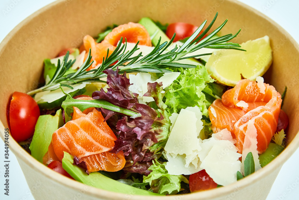 Salad with salmon and cherry tomatoes, lemon, avocado, cucumber, lettuce, arugula, Parmesan cheese, a sprig of rosemary in a cardboard box Salad with salmon and cherry tomatoes, lemon, avocado, cucumber, lettuce, arugula, Parmesan cheese, a sprig of rosemary in a cardboard box