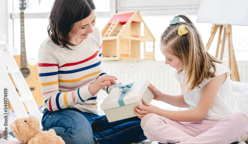 Smiling mother with pretty girl opening beautiful present