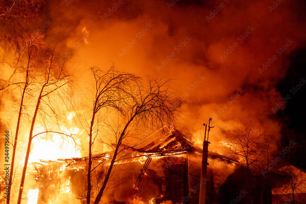 Fire, burning old house at night, flames engulfed the entire house, in the sky the glow of fire