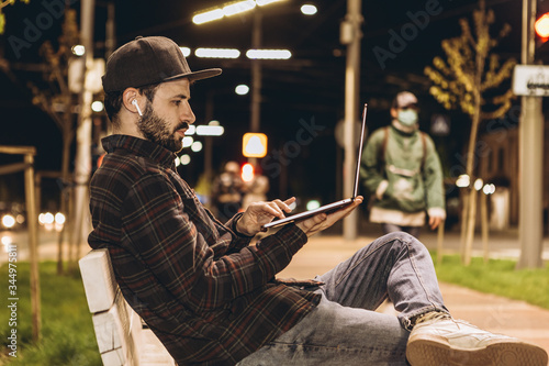 A freelancer with a laptop in his hands works at night on the street, connecting to a public wai fai