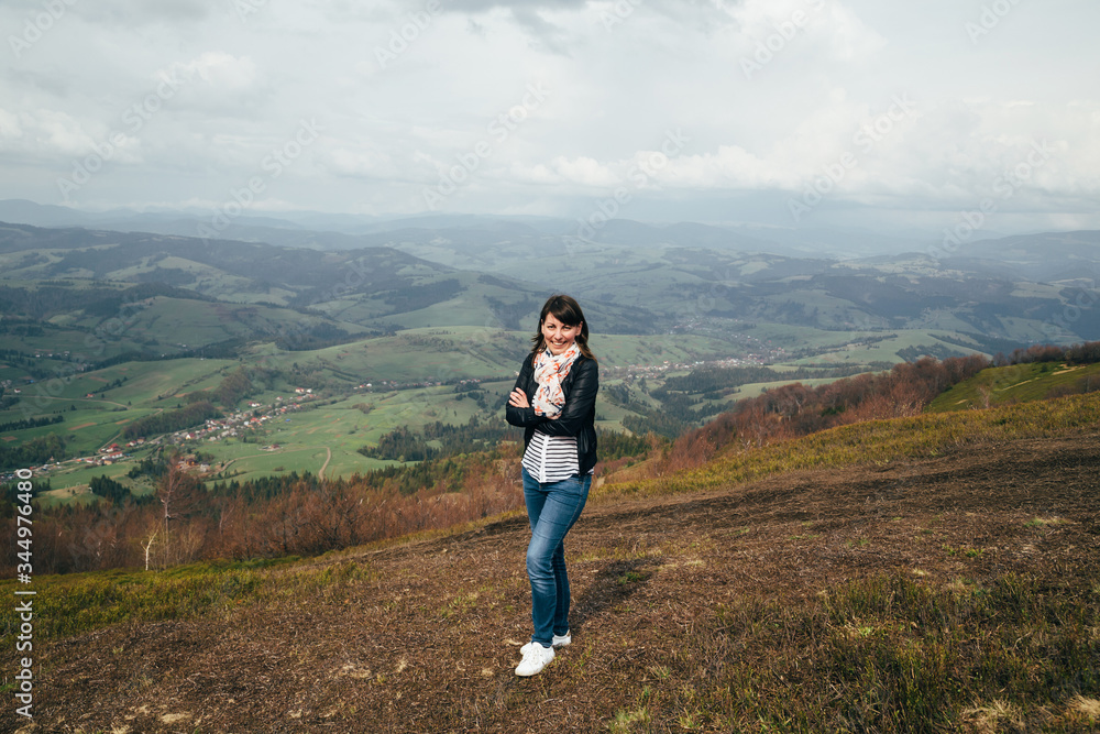 Happy smiling tourist girl in blue jeans and striped shirt hiking up in mountains enjoying silence and harmony of nature Happy smiling tourist girl in blue jeans and striped shirt hiking up in mountains enjoying silence and harmony of nature