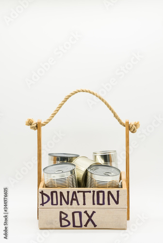 Donation box from light wood with rope handle. Food supplies of canned food, peas and corn, food stock for quarantine, isolation period on white. Donation, coronavirus 