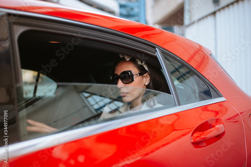 Beautiful caucasian businesswoman with sunglasses sits in the back seat in a red car
