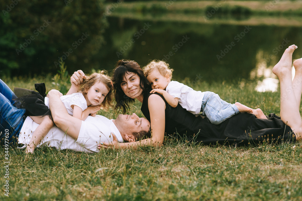 Naklejka premium Handsome young father and beautiful mother in sunny summer nature playing with their cute small childrens