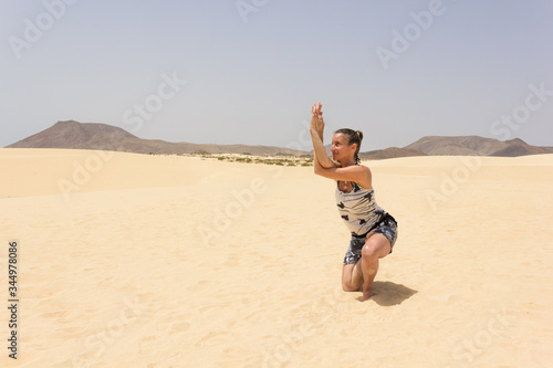 Flexible woman doing vatayanasana yoga asana on empty desert in Corralejo Natural Park. Female yogi performing horse face pose at sand dunes on hot, sunny day in Fuerteventura island, Spain photo