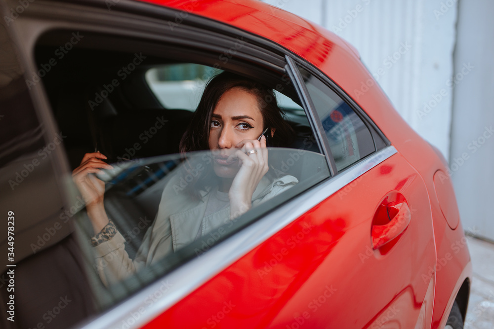 A beautiful caucasian businesswoman with a phone in her hand sits in a red car