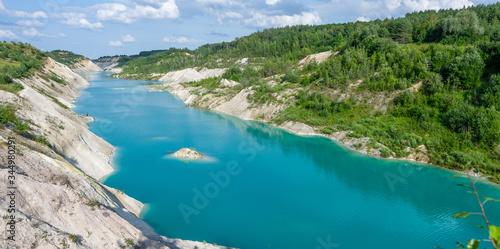 Turquoise river between small mountains with forest. Amazing summer landscape with blue sky and white clouds. Paradise place for romantic travel, to dream in silence looking into deep clear water.