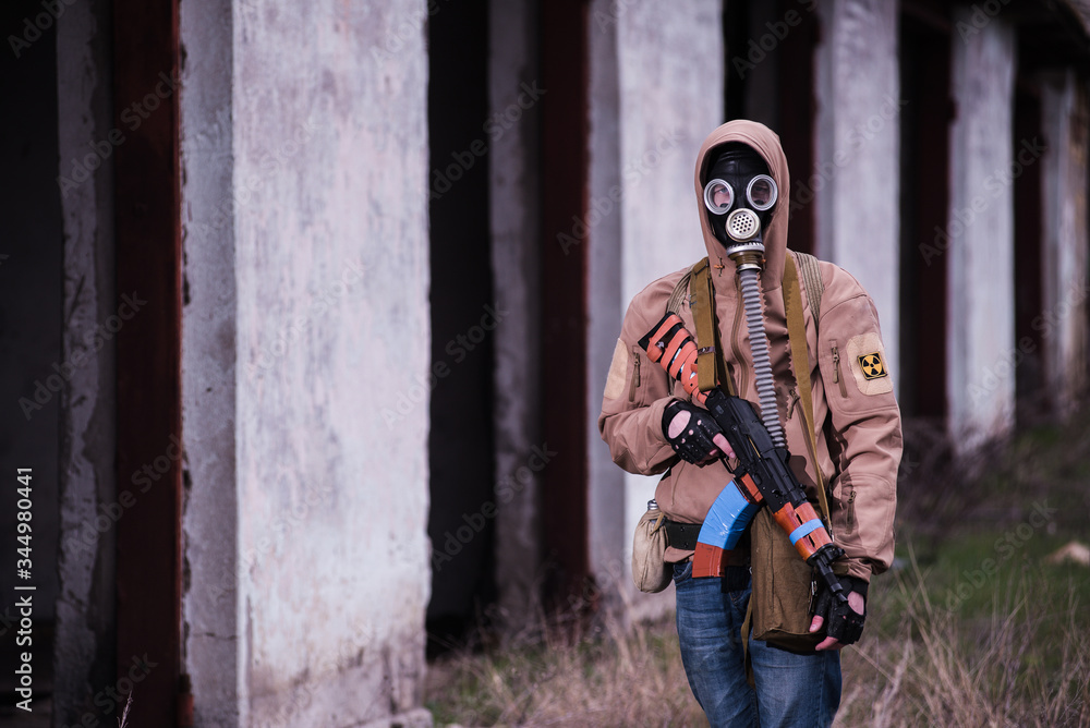 Fototapeta premium Armed stalker warrior in gas mask in front of lost destroyed building