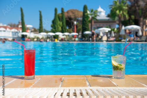Two refreshing cocktails Mojito and Cosmopolitan stand on the edge of the pool in the summer heat with a blurred background. The concept of rest and travel is an expensive holiday. place for text.