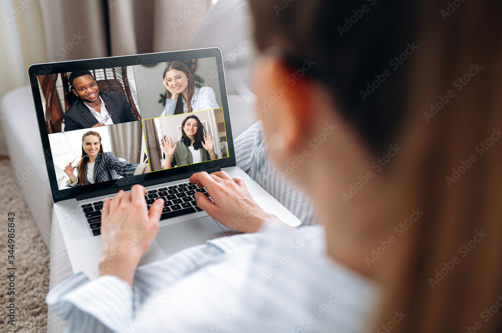 Business team working from home in a video conference. The back view of a girl who communicates online by video conference with her work colleagues using a laptop. Zoom conference