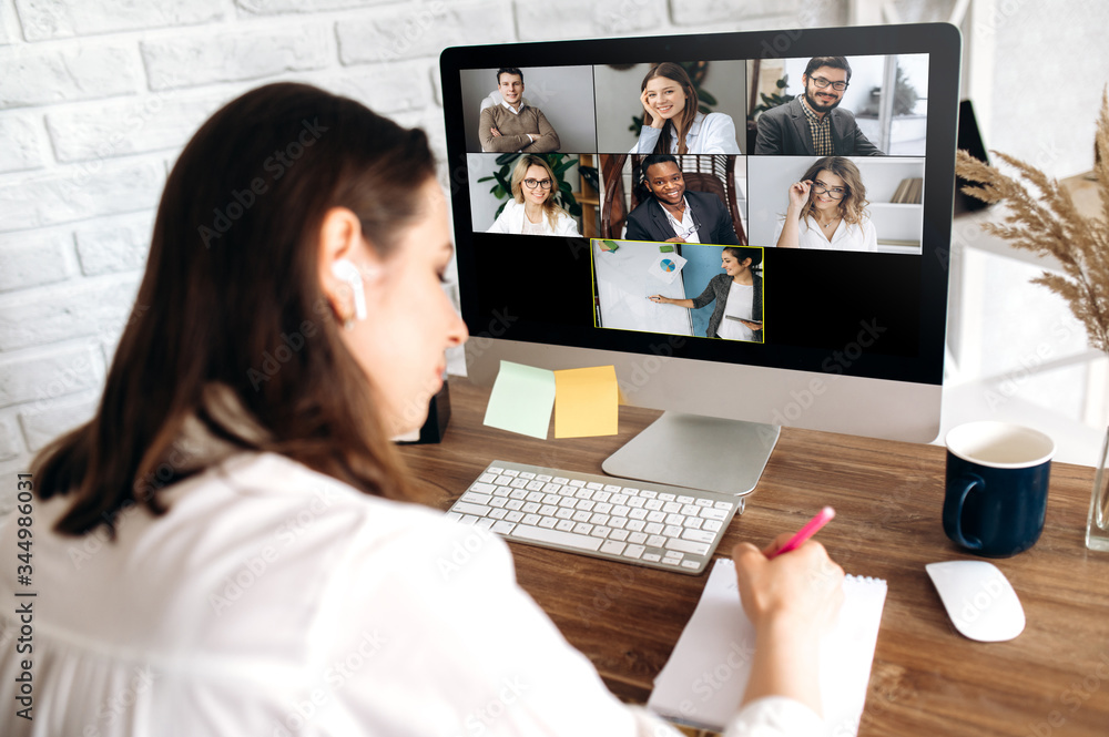 Online training. The back view of a girl who learns online by video conference online. On the screen, the teacher tells the information to her and other participants in the conference Online training. The back view of a girl who learns online by video conference online. On the screen, the teacher tells the information to her and other participants in the conference