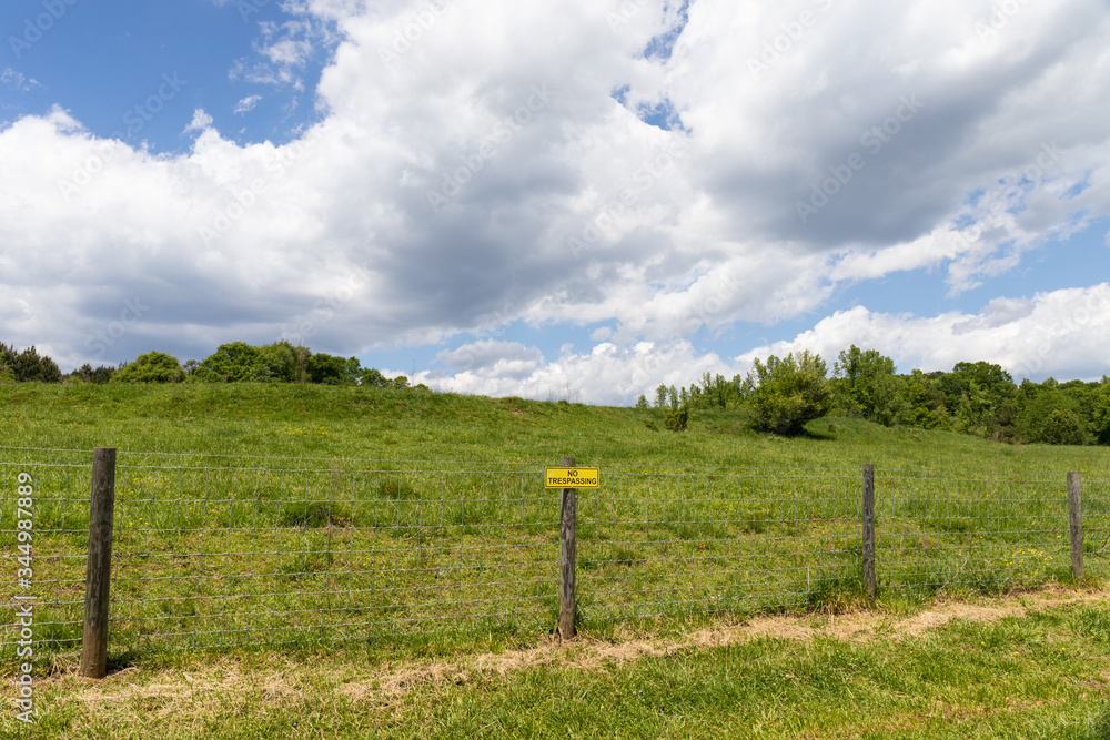 No Trespassing sign on a barbed wire fence, lush green pasture beyond, implied privilege, horizontal aspect