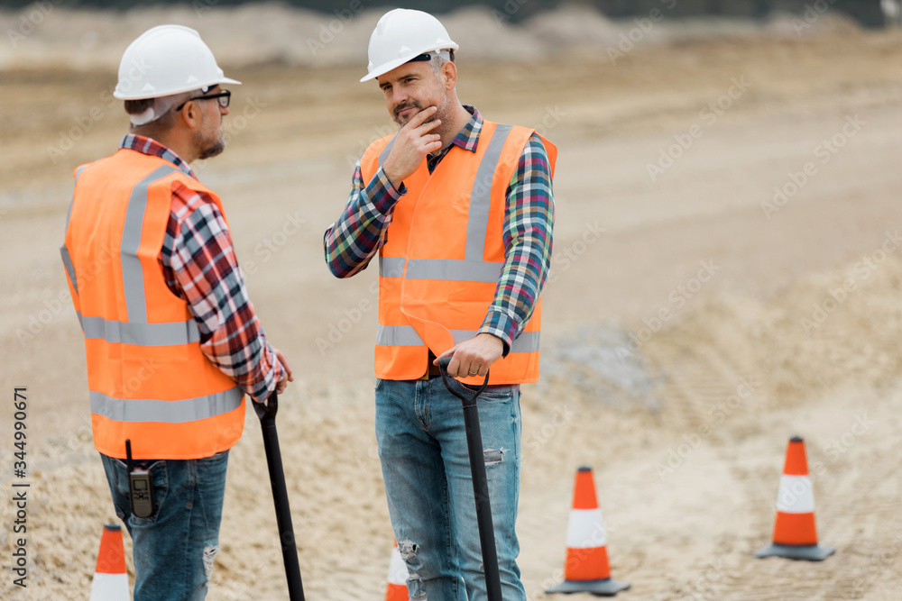 Two professional road construction workers in orange vests and protective helmets in the middle on the terrain