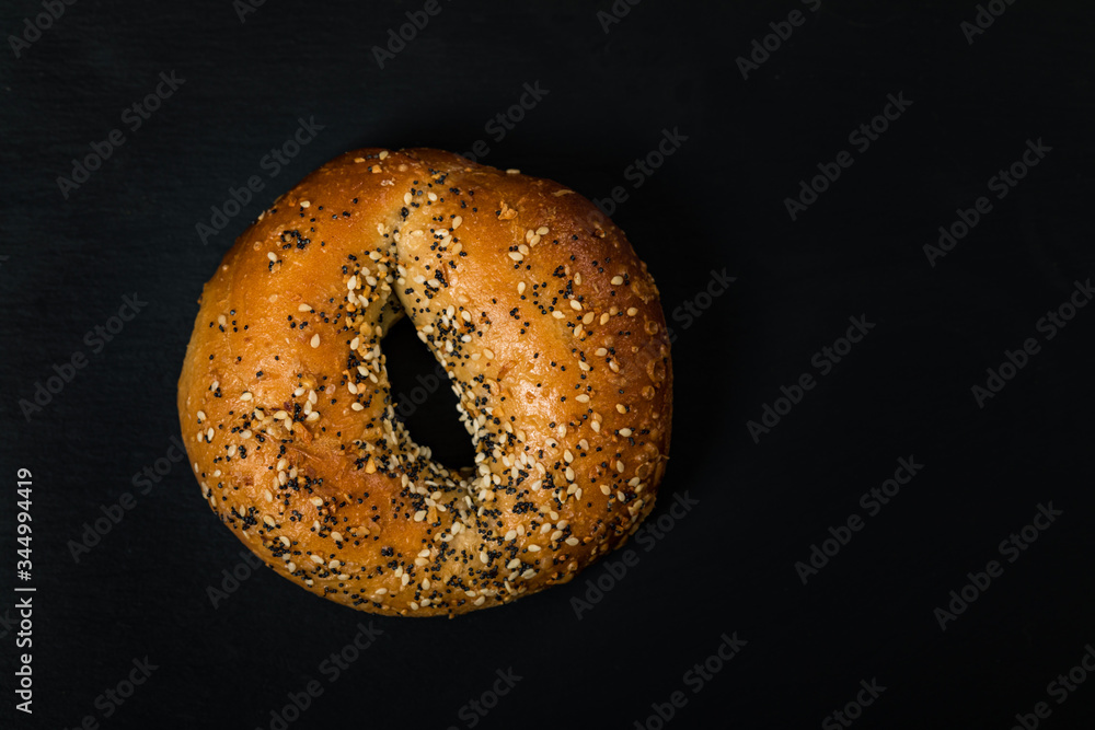 Freshly Baked Bagels Topped with Sesame Seeds, Poppyseeds, Garlic and Onion on Black Background. Selective focus.