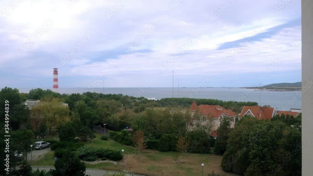 view from the balcony of the house with a rank roof standing among the trees on the seashore near the high striped lighthouse view from the balcony of the house with a rank roof standing among the trees on the seashore near the high striped lighthouse