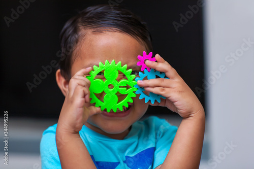 A hispanic boy having fun as he holds a gear set and learns about engineering in a exploratory problem solving environment.