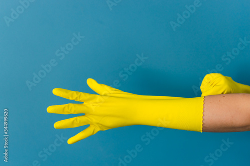 Close up on hand of unknown caucasian woman female girl putting on adjusting holding protective yellow rubber gloves to clean or disinfection against blue wall background in day