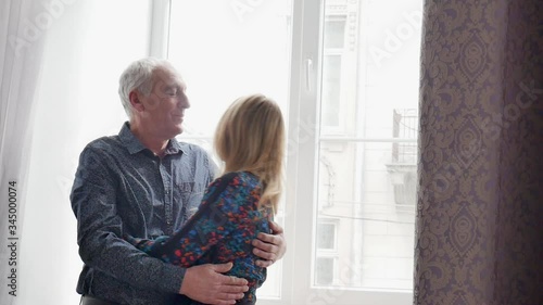 Close up portrait of elderly man and his young blonde-haired wife embracing each other indoors. Couple with age difference.