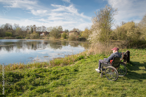 Old man in a wheelchair overlooking a calm lake on a warm afternoon Hampshire UK