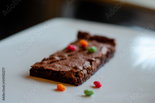 Homemade brownie on white plate. Brownie on black counter. Brownie with decoration. Brownie with smiley.