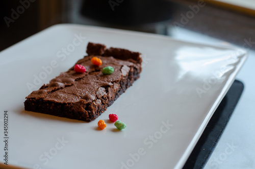Homemade brownie on white plate. Brownie on black counter. Brownie with decoration. Brownie with smiley.