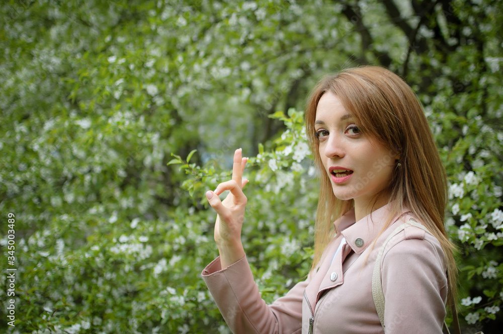 Blonde woman is showing ok on flowering tree background in the garden during early spring. Stop allergy concept Blonde woman is showing ok on flowering tree background in the garden during early spring. Stop allergy concept