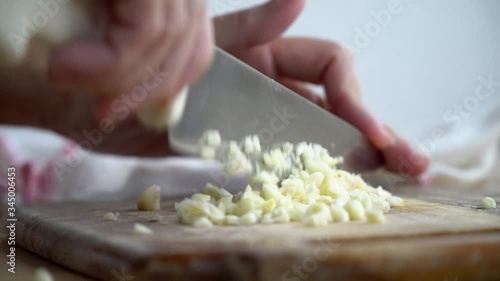Close up of a woman's hands chopping garlics on wooden chopping board in kitchen. 
