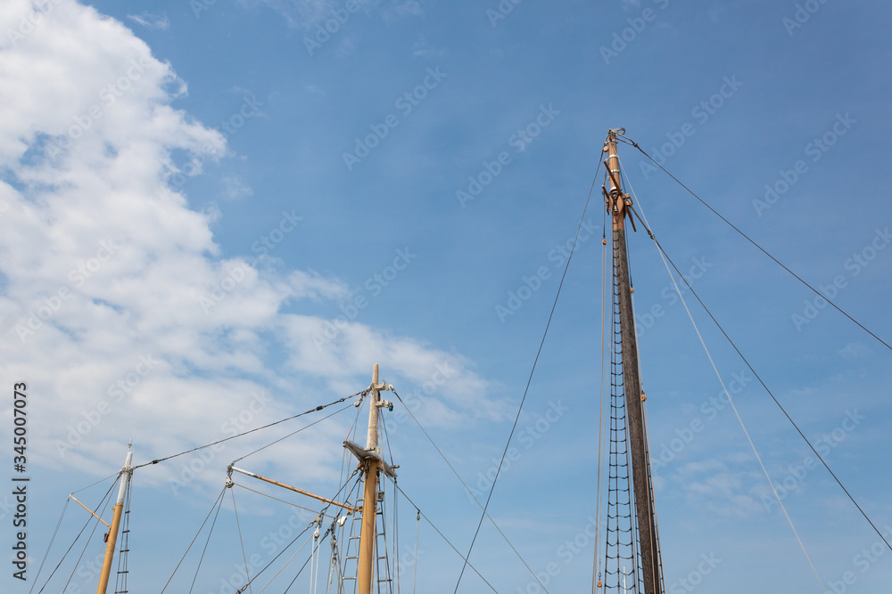 Three masts from two different sailing vessels against a blue sky with clouds, nautical backdrop with copy space, horizontal aspect