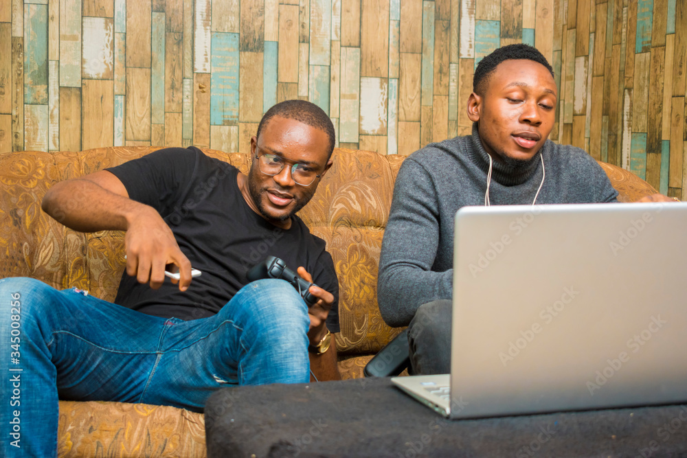 two handsome africans guys sitting on the couch playing video games with joystick, game pad, pad two handsome africans guys sitting on the couch playing video games with joystick, game pad, pad
