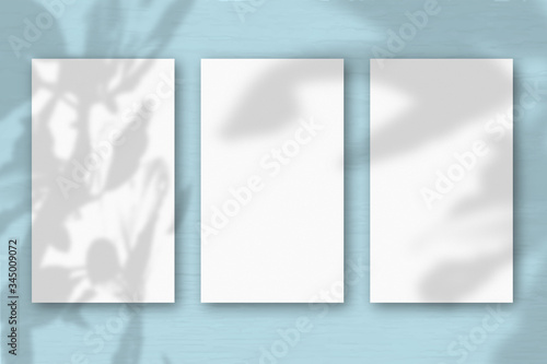 3 vertical sheets of textured white paper on soft blue green table background.Mockup overlay with the plant shadows. Natural light casts shadows from an exotic plant. Horizontal orientation