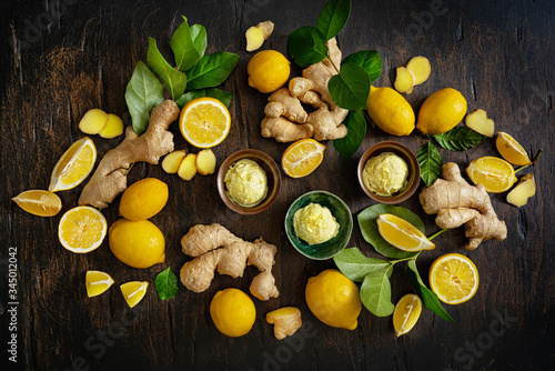 Homemade lemon and ginger ice cream in ceramic cups and fresh fruit and lemon leaves and ginger roots on a dark wooden background. Cold summer dessert concept. Top view