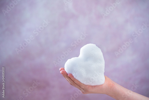 The child's hands hold soap foam in the shape of a heart. Soap heart and pink Gerber flower on a ceramic background. Hand hygiene as coronavirus protection. Antivirus and antibacterial concept