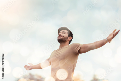 Happy Traveler male embracing life and enjoying freedom with open arms over sky and bokeh effect. Carefree smiling Bearded man standing relaxing and breathing fresh nature air at outdoor. Healthy life