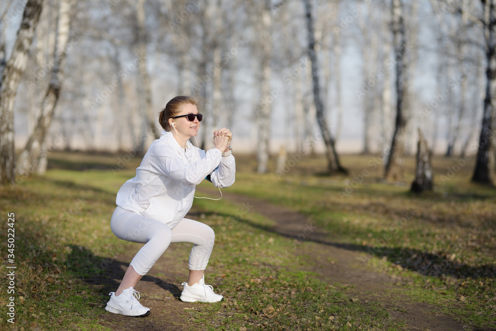 Sporty woman doing squat morning exercise alone in park. Sporty woman doing squat morning exercise alone in park.